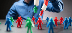 A close-up image of a person in a blue shirt holding a large red-and-white magnet, attracting small colorful figurines representing customers. The figurines are green, red, and blue, symbolizing diverse customer engagement and successful marketing efforts.