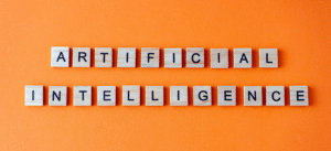 A close-up image of wooden letter tiles spelling out 'ARTIFICIAL INTELLIGENCE' on a bright orange background. The tiles are neatly arranged, emphasizing the concept of AI in a simple yet vibrant design.