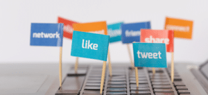 A close-up image of colorful flags with social media-related words like 'like' and 'tweet,' placed on a laptop keyboard. The flags represent engagement and interaction on social media platforms, emphasizing online presence and activity.