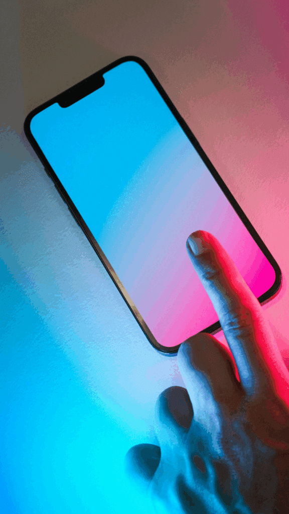 Close-up of a finger about to tap a smartphone screen illuminated with blue and pink light, representing digital indexing and mobile interaction relevant to Google Gemini.