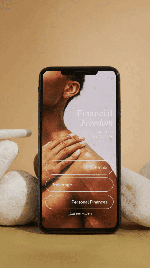 Close-up of a smartphone displaying a financial app landing page with a person’s hand on their shoulder. The screen features the text 'Financial Freedom is at your fingertips' and buttons labeled Stocks, Brokerage, and Personal Finances.
