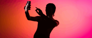 Silhouette of a person taking a selfie with a smartphone in front of a vibrant pink and orange gradient background, symbolizing digital personalization and modern content marketing trends.