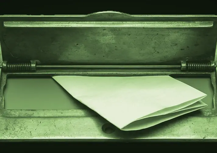 A brass mail slot with a folded note pushed through it.
